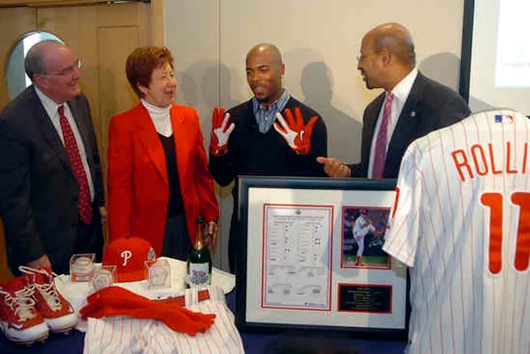 PHILLIES shortstop Jimmy Rollins (in gloves) is joined by team president David Montgomery (left) in presenting Rollins' 2008 championship-season uniform and other team memorabilia to the Atwater Kent Museum during a news conference yesterday at the Independence Visitors Center. Accepting the donations were Mayor Nutter and museum CEO Viki Sand.