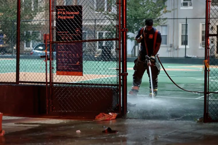 A Philadelphia firefighter washes blood away from one of the crime scenes on a basketball court at the 8th and Diamond Playground in North Philadelphia, the site of the quadruple shootings.