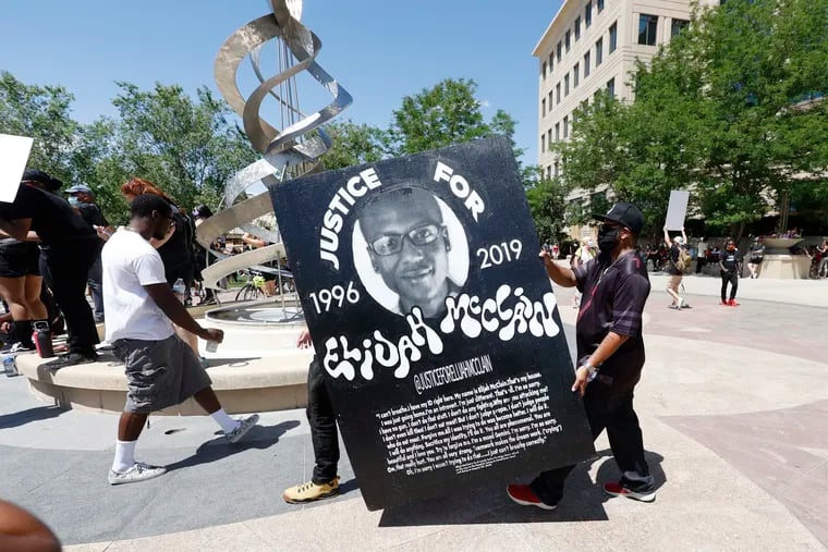 This June 27 photo shows demonstrators carrying a giant placard during a rally and march over the death of 23-year-old Elijah McClain outside the police department in Aurora, Colo.