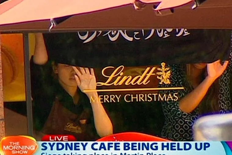 This image taken from live television in Sydney shows people holding up a black banner with Arabic writing on it inside the Lindt Chocolat Cafe Monday.