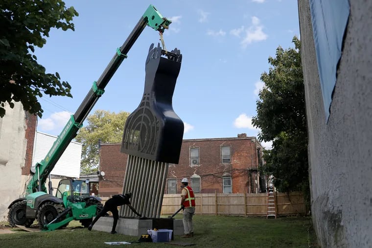 Workers install a 28-foot-tall version of Hank Willis Thomas' sculpture "All Power to All People" along 52nd Street at Arch Street in West Philadelphia on Wednesday.