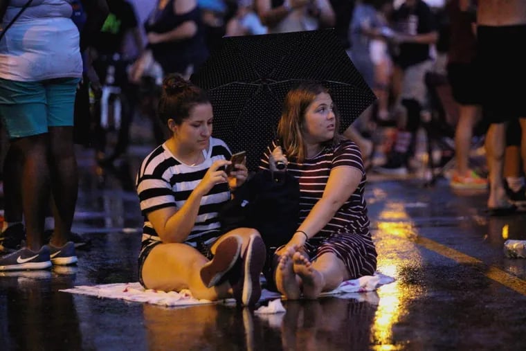 Janae Metzler (left) and Erika Stover sit on the ground along the Benjamin Franklin Parkway  after rainfall earlier this month.