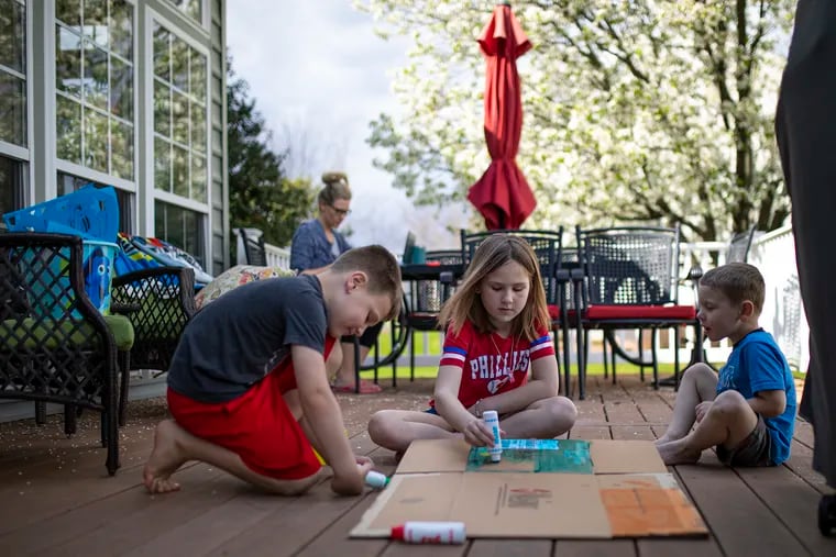 Cameron Mocey, 5, left, Sienna Mocey, 7, center, and Nathan Mocey, 4, right, help each other decorate a box on the back deck of their home on Wednesday, April 8, 2020. The three were supposed to be going to Disney World with their parents, grandparents, aunts and cousins, but the coronavirus canceled the trip.
