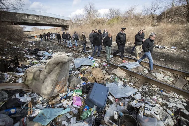 Politicians, law enforcement personnel and reporters tour an open air drug market strewn with litter and used needles, along train tracks in Kensington.