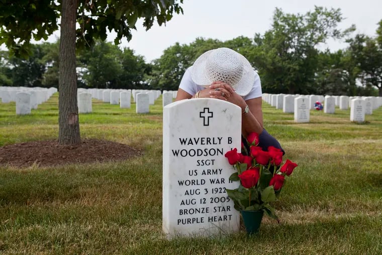 In this undated photo, Joann Woodson kneels at the grave of her husband, Cpl. Waverly B. Woodson Jr., at Arlington National Cemetery in Arlington, Va. Woodson, a member of the only African American combat unit to land at Normandy, saved dozens of wounded troops on D-Day despite being severely injured himself.