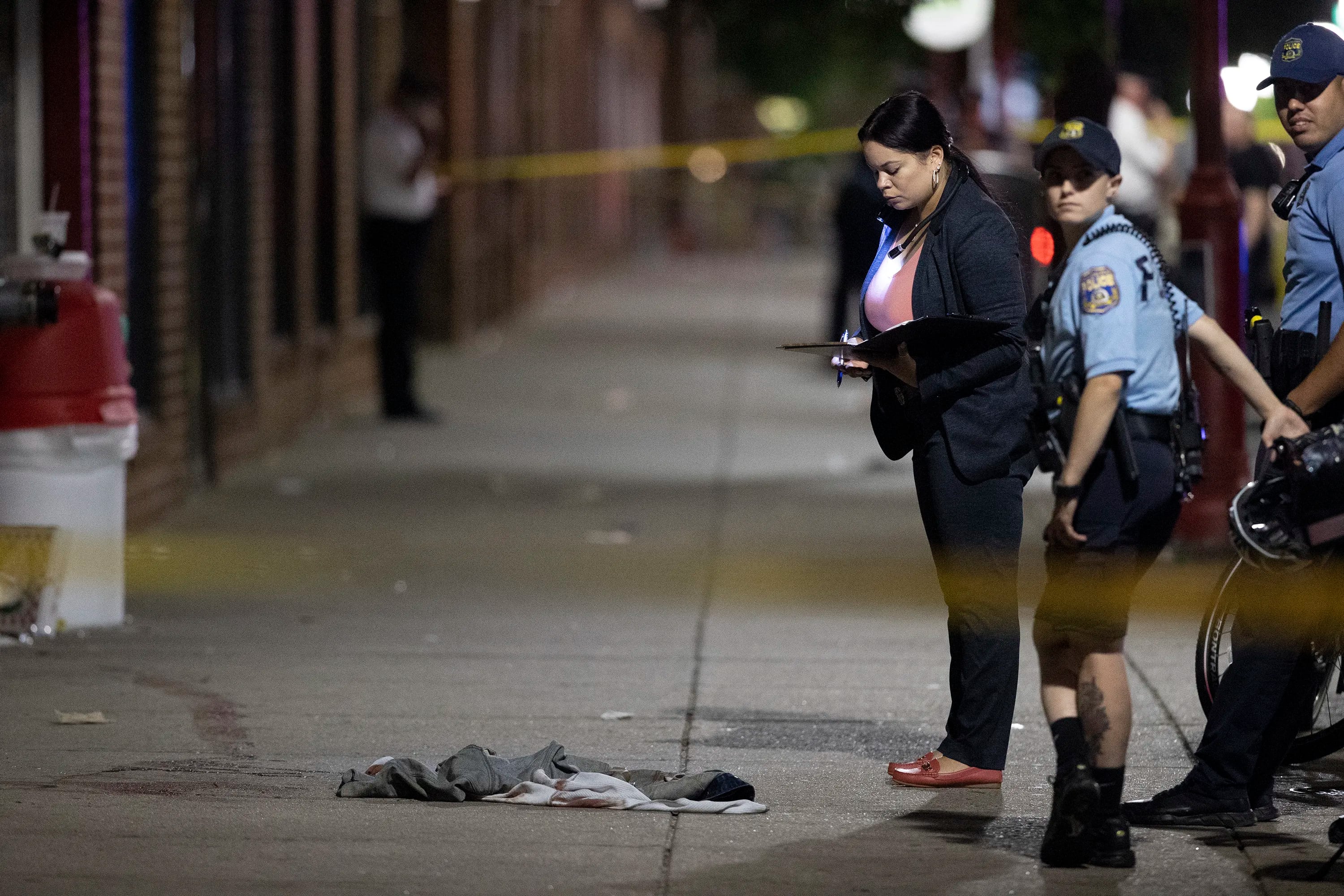 Philadelphia Police officers and detectives look over evidence at the scene of a shooting on and near South Street that left 3 dead and 11 wounded.
