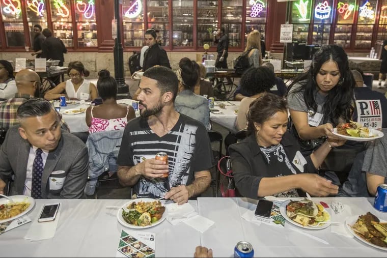 A diverse group of diners partakes in the food prepared for the “Breaking Bread, Breaking Barriers”  dinner Monday night on Filbert Street, outside Reading Terminal Market.