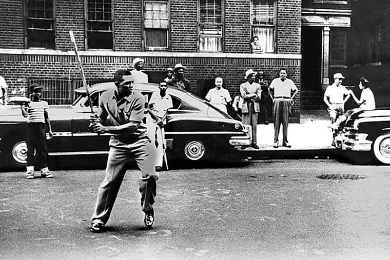 Full length action batting portrait of Hall of Famer, Willie Howard Mays in street clothes, playing stickball in Harlem, NY, c. 1950's with bystanders and tenements in background. (Handout photo)