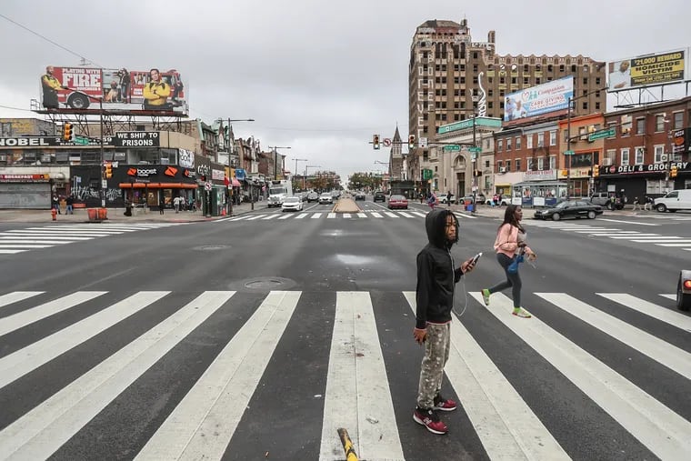 Pedestrians cross the overscaled intersection at Broad Street and Erie Avenue at rush hour.