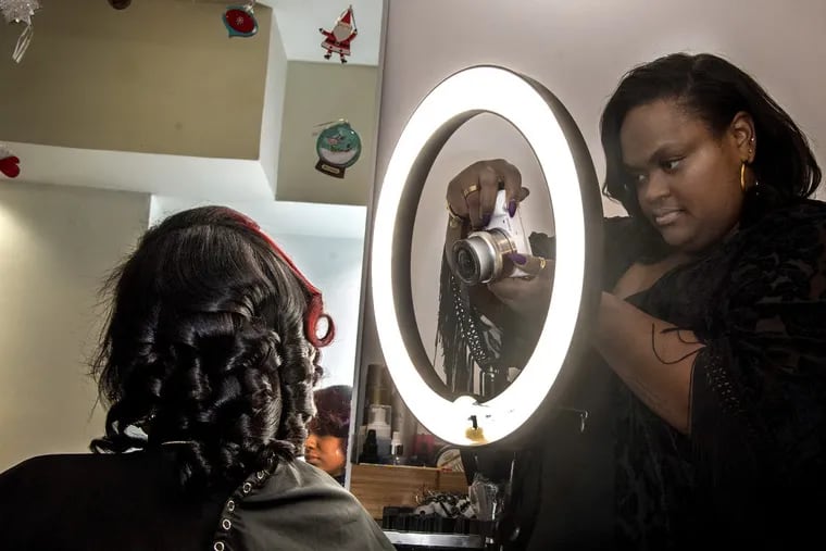 Kee Taylor (right), 34, owner of the West Philly salon Deeper than Hair, photographs client Ryan Brooks. Taylor has cultivated a national fan base through posting photos of her salon’s work on social media. CLEM MURRAY / Staff Photographer