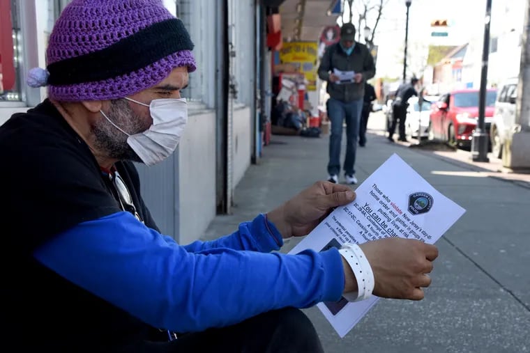 David Rivera reads a coronavirus flier handed out by Camden County police officers Sunday along Federal Street in East Camden.