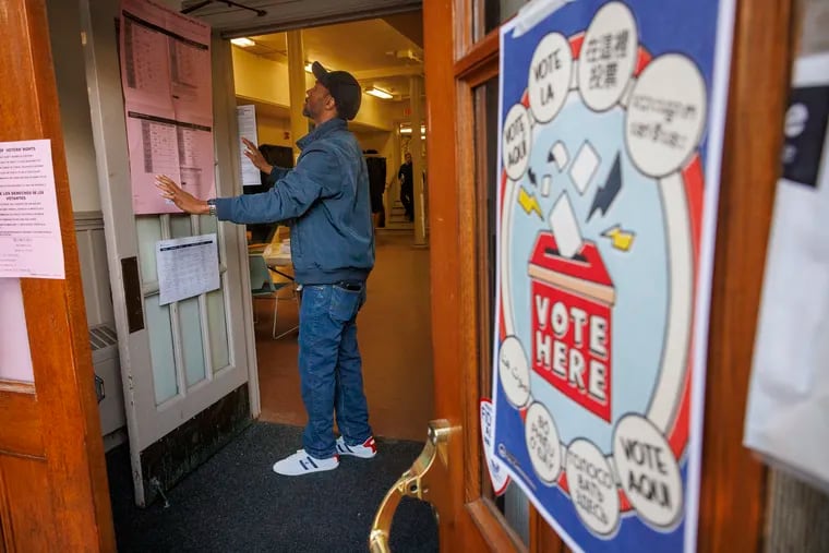 Christopher Coleman hangs voter information on doors leading to polling station inside the Free Library Falls of Schuylkill Branch in East Falls section of Philadelphia on Tuesday, April 23, 2024.
