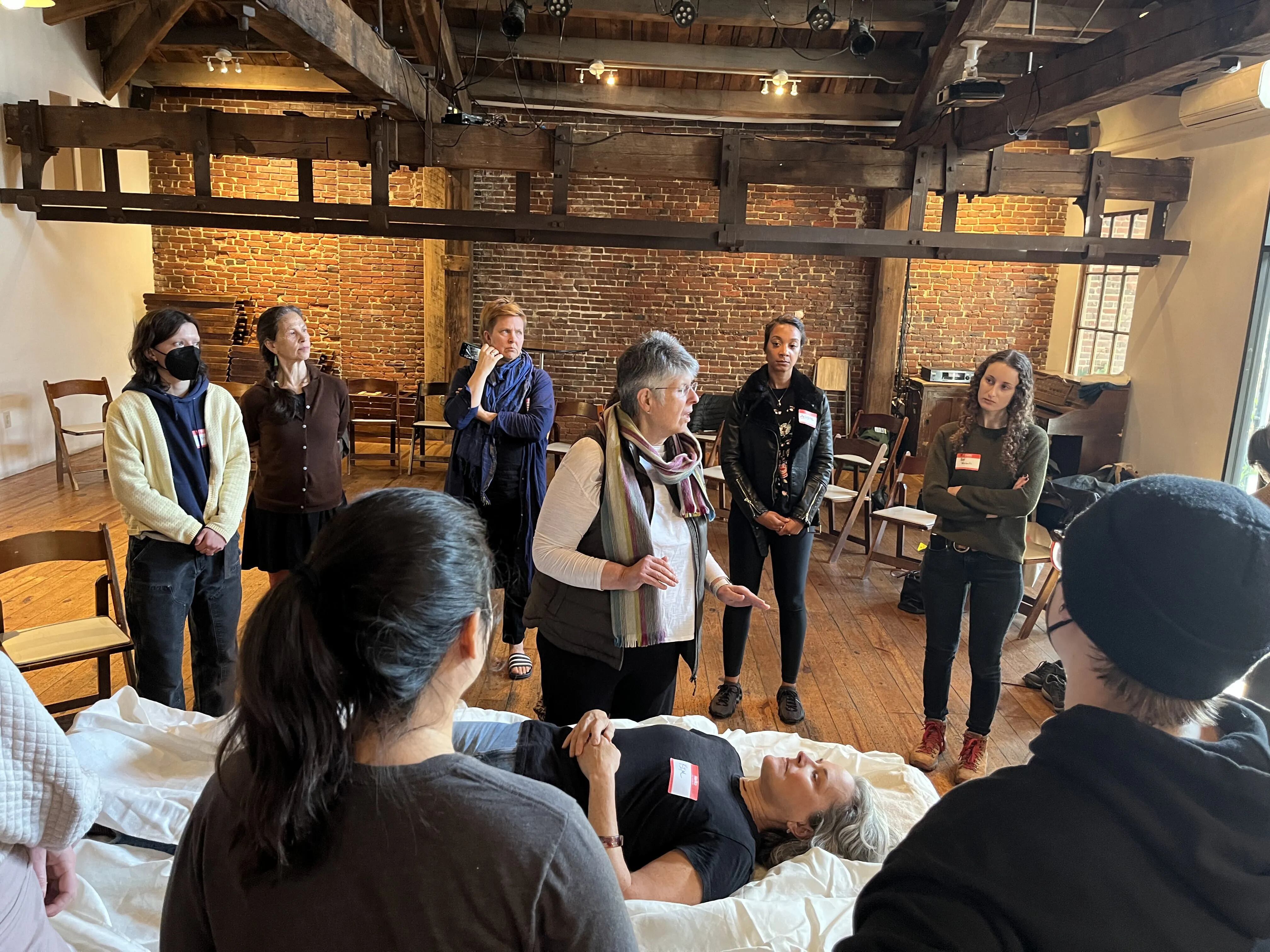 Pat Quigley, center and funeral director at Laurel Hill cemetery, teaches attendees how to shroud a dead body at a recent workshop in Northern Liberties. Kim Schmucki, on the table, volunteered to be practiced on.
