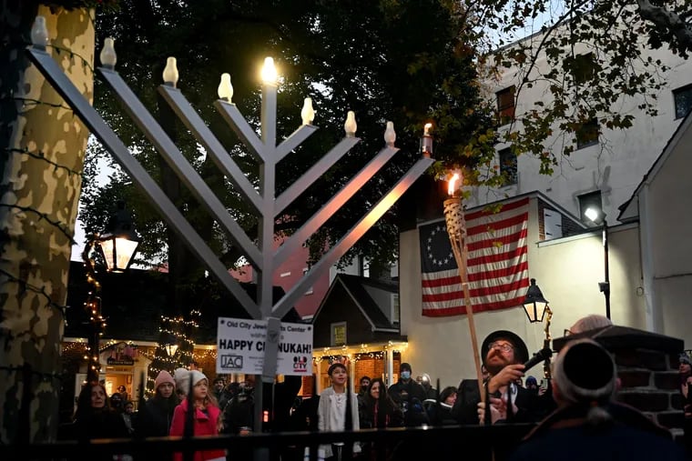 Rabbi Zalman Wircberg (right) with the Old City Jewish Arts Center watches as the first candle is lighted — using a real flame and real oil lamp — on the community menorah at the Betsy Ross House on the first night of Hanukkah, Nov. 28, 2021.