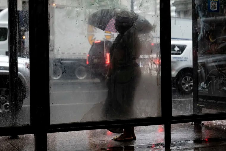 A person stands at a bus stop on Broad Street near City Hall during a rainstorm in Philadelphia on Friday.