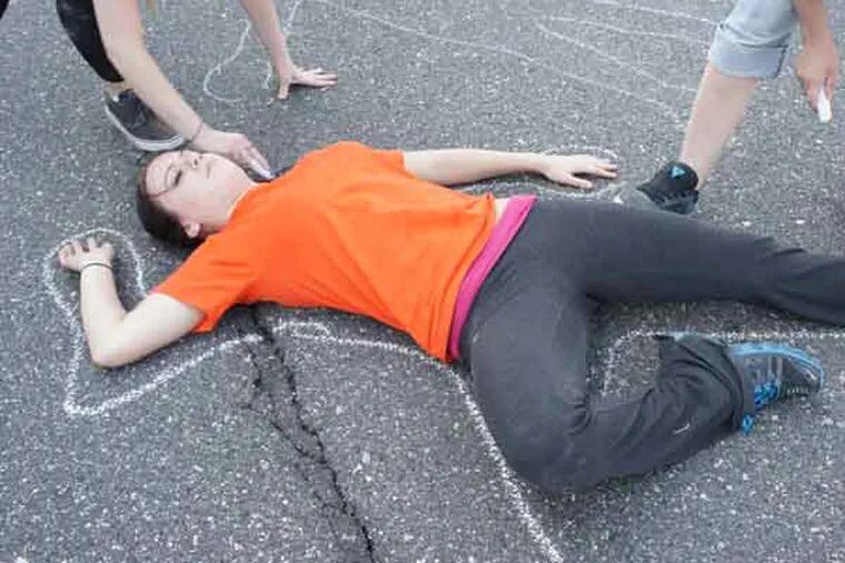 Danielle Goodhart, 21, lies on the ground Saturday while Ally Super, 19 (left) and Faith Mohnke, 20 draw a chalk outline around her to represent one of 2013’s gun violence victims. Students and volunteers drew thousands of the outlines on JFK Boulevard between 20th and 30th Streets for a public art project, “American Casualties: A Chalk Drawing.” Staff photo by Jonathan Lai