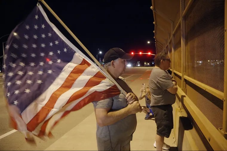 Joe Gruber, of Anthem, Ariz., holds an American flag at an overpass along Interstate 17 as he and dozens of others wait for the procession with the hearse carrying the late Arizona Sen. John McCain, Saturday, Aug. 25, 2018, in Anthem, Arizona.