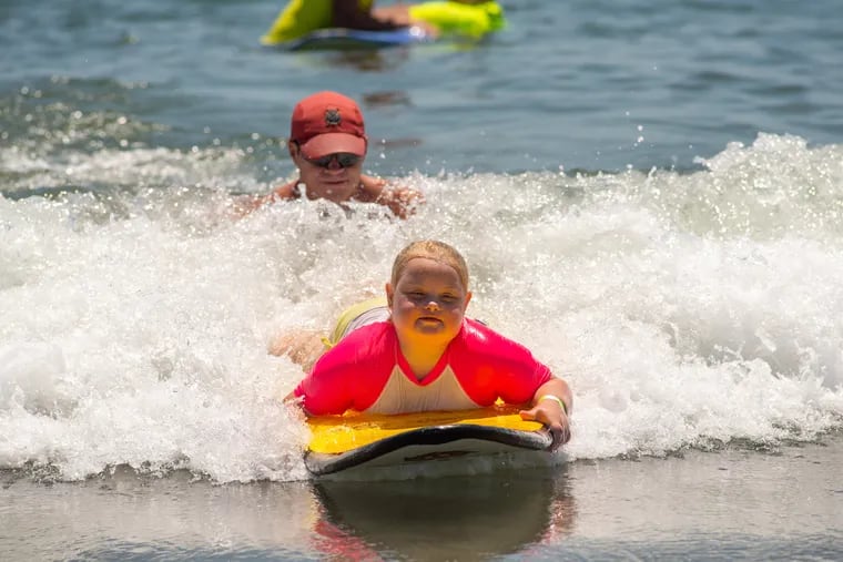 Lifeguard Ryan Comas, 20, of Philadelphia pushes Sage Praweckyj, 8, on her paddle board during the 11th annual 21 Down Beach Day at Schellenger Street beach in Wildwood. Every summer, the Wildwood Beach Patrol opens Lincoln Avenue Beach for kids with Down syndrome and their families for 21 Down Beach Day. On this day, these children swim with seasoned Wildwood lifeguards on soft-top paddleboards.