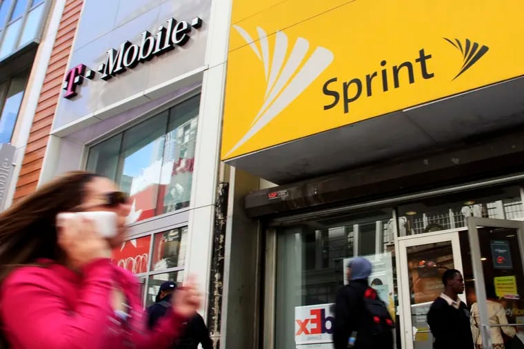 A woman using a cell phone walks past T-Mobile and Sprint stores in New York.