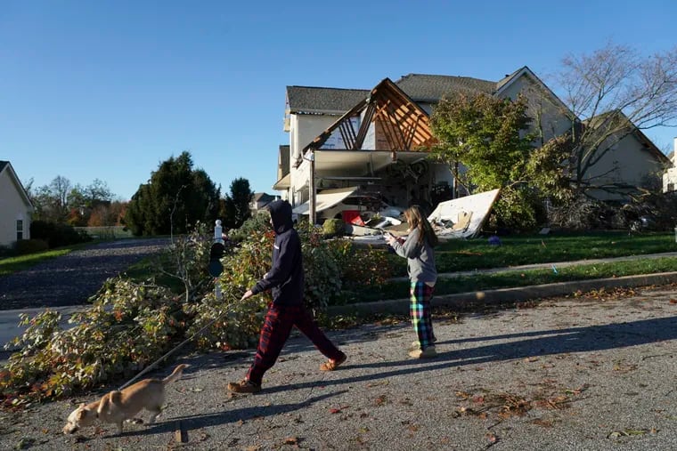 Shane Wilson (left) and sister Noelle Wilson walk their dog Auggie past a damaged house from Thursday's storm in Thornbury Township, Delaware County.