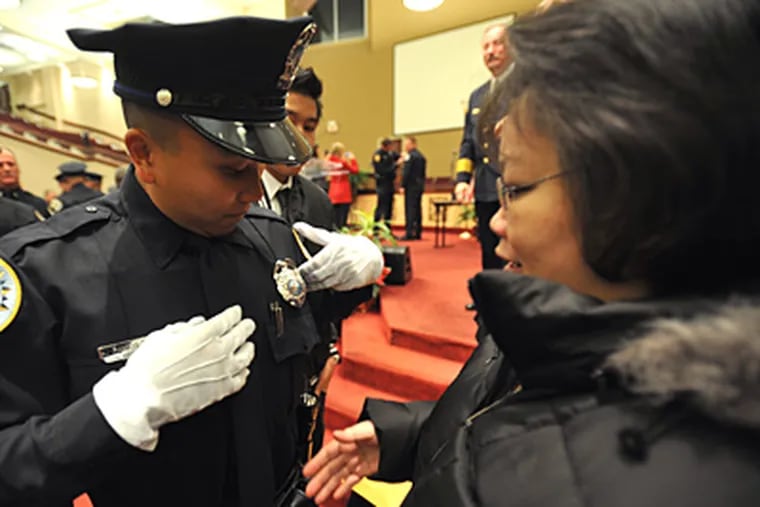 Ex-Camden Officer Alejandro Ramos looks at his new badge after his mother, Nommita, pinned it on. He had just graduated from the Nashville Police Academy. (Christopher Berkey / For The Inquirer)