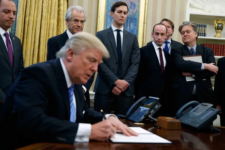 White House Chief of Staff Reince Priebus (from left), National Trade Council adviser Peter Navarro, Senior Adviser Jared Kushner, policy adviser Stephen Miller, and chief strategist Steve Bannon watch as President Trump signs an executive order in the Oval Office of the White House.