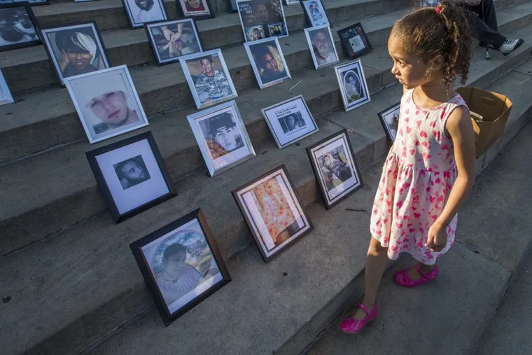 Elisha Sharpe walks by photos of the victims of gun violence placed on the Art Museum steps on June 15