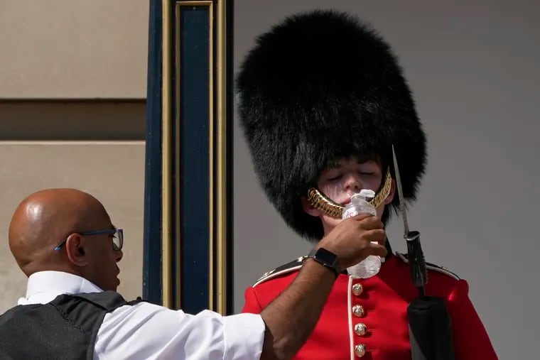 A police officer gives water to a British soldier, wearing a traditional bearskin hat, on guard duty outside Buckingham Palace during hot weather in London on Monday.