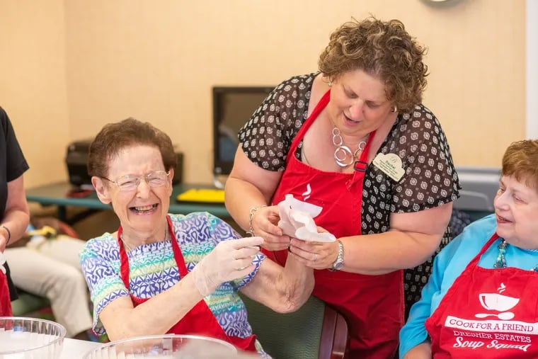 Rachel Kaufman Schatz (middle) helps Evelyn Schwedock, 87, (left) put on her gloves as the Soup Squad at Brandywine Living at Dresher Estates prepares to make vegetable soup. Once a month, the residents get together to make soup for seniors who need food while living at home. Suzi Kaufman, 81, right, was one of the group's original members.