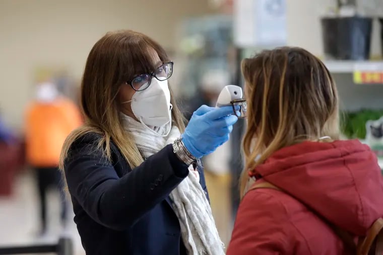 An employee test customers' body temperature at the entrance of the Esselunga supermarket, in Milan, Italy, Wednesday, March 25, 2020. The new coronavirus causes mild or moderate symptoms for most people, but for some, especially older adults and people with existing health problems, it can cause more severe illness or death.