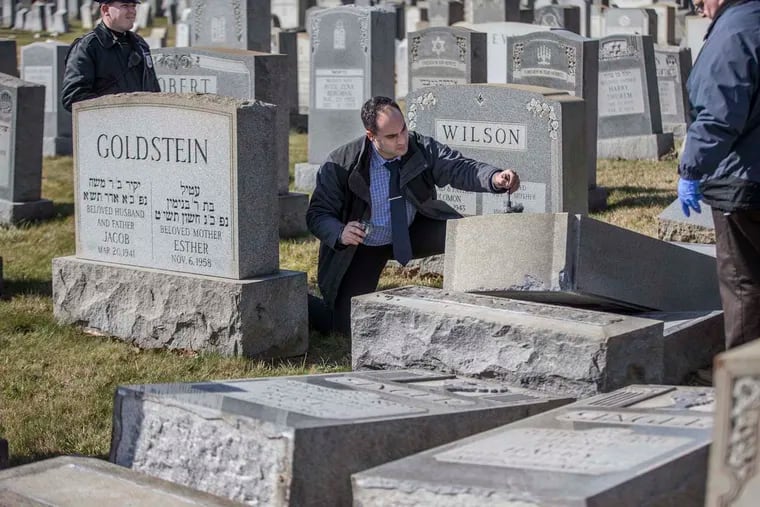 Northeast Philadelphia Police Dectective Timothy McIntyre, center, dusts for fingerprints on one of the many headstones that were vandalized at the Jewish Mount Carmel Cemetery. Estimates are that around 100 headstones were pushed over or broken. The damage was discovered Sunday morning, Feb. 26, 2017.