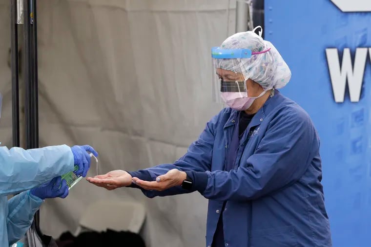In this March 17, 2020, photo, Theresa Malijan, a registered nurse, has hand sanitizer applied on her hands after removing her gloves after she took a nasopharyngeal swab from a patient at a drive-thru COVID-19 testing station for University of Washington Medicine patients in Seattle.