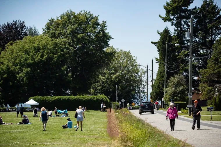 A ditch marks the Canada-U.S. border and separates people walking on the road, right, in Surrey, British Columbia, and those gathered at Peace Arch Historical State Park, left, in Blaine, Wash.
