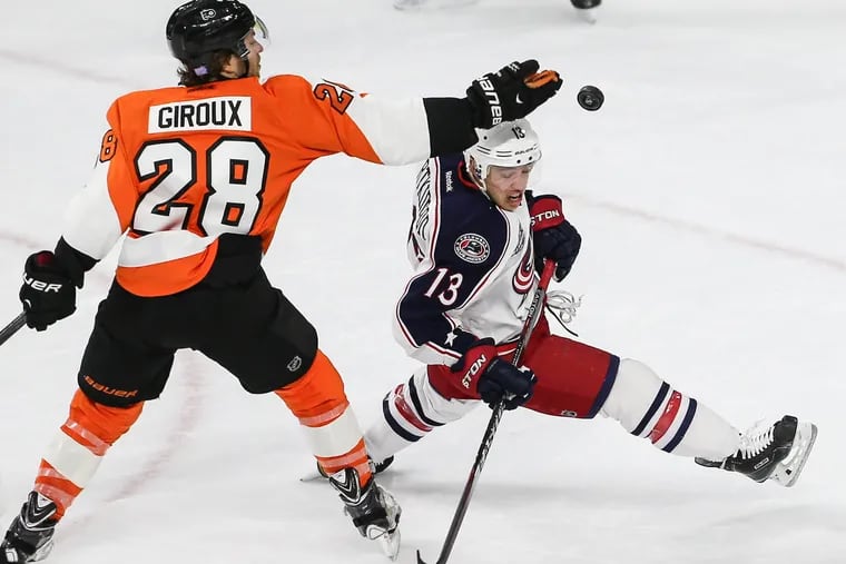 In a file photo, the Flyers' Claude Giroux tries to bat the puck down over the Blue Jackets' Cam Atkinson.