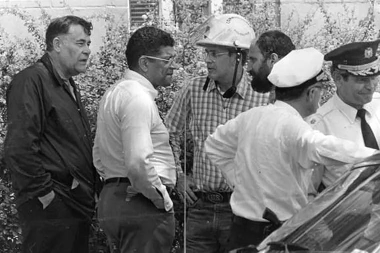 On May 13, 1985, Police Commissioner Gregore J. Sambor, Managing Director Leo A. Brooks, and Fire Commissioner William C. Richmond (in white helmet) meet with other officials at command post near the MOVE compound.