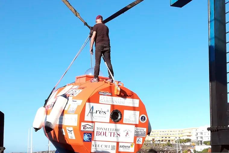 In this photograph taken Saturday Dec. 22, 2018, Frenchman Jean-Jacques Savin, 71-year-old, stands on top of his 3-metre (10-foot) long, 2.1-metre (7-foot) wide resin-coated plywood capsule, which will use ocean currents alone to propel him across the sea. Savin set off from El Hierro in Spain's Canary Islands on Wednesday and is aiming to complete his 4,500-kilometre (2,800-mile) journey to the Caribbean in about three months. (Courtesy of Jean-Jacques Savin via AP)