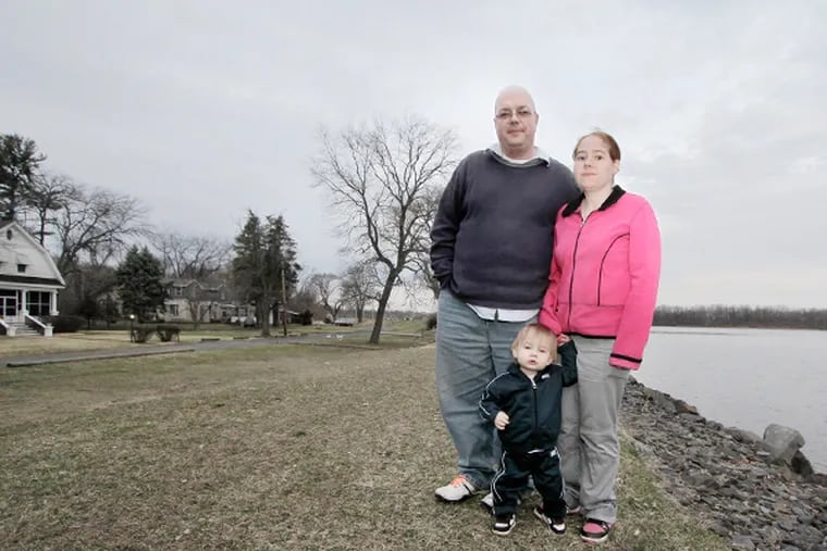 John Delancey III, wife Jennifer Delancey and 15-month-old John Delancey IV pose on the levee that stands between their Bristol home and the Delaware River on April 3, 2014. (ELIZABETH ROBERTSON/Staff Photographer)
