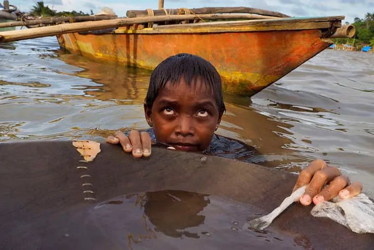 Jonathon Ramorez, 12, stands waist-deep in the bay with a wooden pan he uses to separate gold from sediment. He will spend hours in the water, which often is tainted with animal waste and teeming with bacteria. LARRY C. PRICE