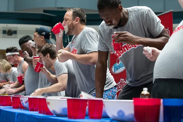 The #1-ranked competitive eater in the world, Joey Chestnut, center, drinking water, eats donuts with other contestants at Liberty Place, in Philadelphia, to compete in the first-ever Hostess Donettes-eating contest, Friday, June 1, 2018. 