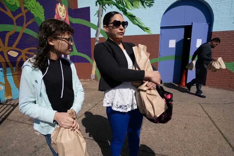 Angeliz Rivera, left, and her mother Liz Del Valle, center, stop and talk with a reporter after picking up lunches at Cramp Elementary School, in North Philadelphia in March. Bowing to national pressure, the USDA will cut red tape to help more students who are learning virtually have school lunch and breakfast.
