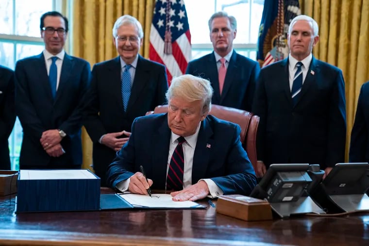President Donald Trump signs the coronavirus stimulus relief package in the Oval Office.