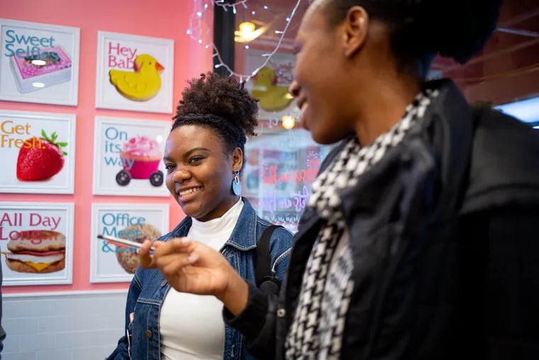 Khanya Branm (left), a senior, and Ayooluwa Ariyo, a junior at Temple University, report for a story about Tiffany's bakery in the 15th Street subway concourse near Temple's Center City Campus last month.