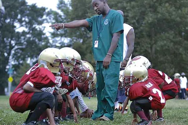 North Philly Aztecs 75 lb coach Roling Davis works with the 4,5 and 6 yr olds during practice in Hunting Park on Aug. 7, 2013. The teams will soon be playing on the nearly completed $1.4 million dollar Team Vick Field in Hunting Park.  ( ELIZABETH ROBERTSON / Staff Photographer )