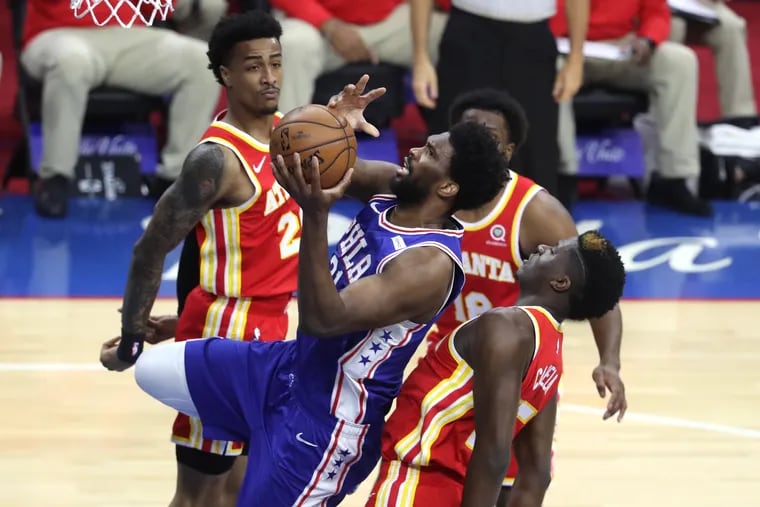 Joel Embiid, center, of the SIxers goes up for a shot between John Collins, left, and Clint Capela of the Hawks during the 1st half of game 2 of their NBA playoff series at the Wells Fargo Center on June 8, 2021.