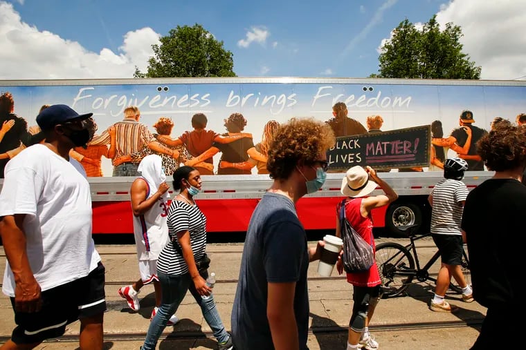 Community members march past a truck trailer with a "Forgiveness bring Freedom" message along Germantown Avenue during the “Too Many Too Mighty” – Marching with a Renewed Mission, Father's Day march.