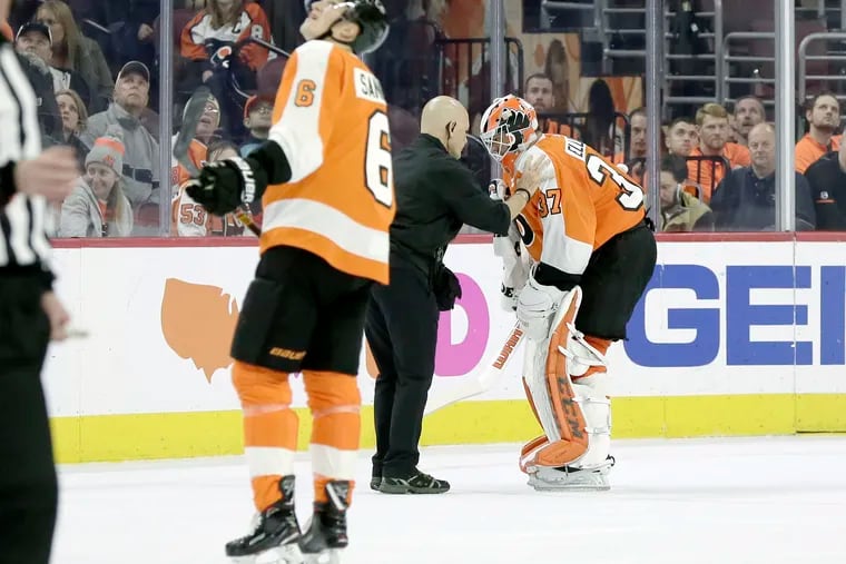 Philadelphia Flyers goalie Brian Elliott is helped off the ice by trainer Jim McCrossin after suffering what appeared to be a groin injury in Thursday's loss to the New Jersey Devils.