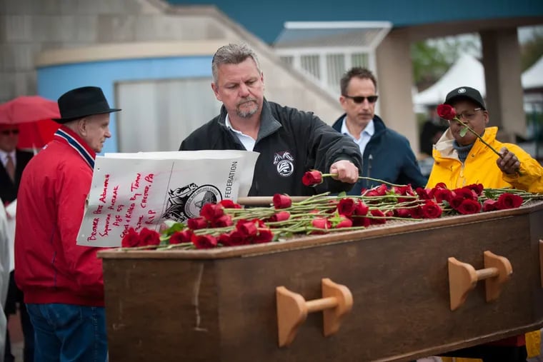 John F. McAteer (center), of Folsom, places a rose on top of a symbolic casket for Pete Adamovich, his co-worker who died in the Amtrak collision on April 3, 2016, during a Workers Memorial Day service at Penn’s Landing. PhilaPOSH will host its annual Workers Memorial Day service Friday.