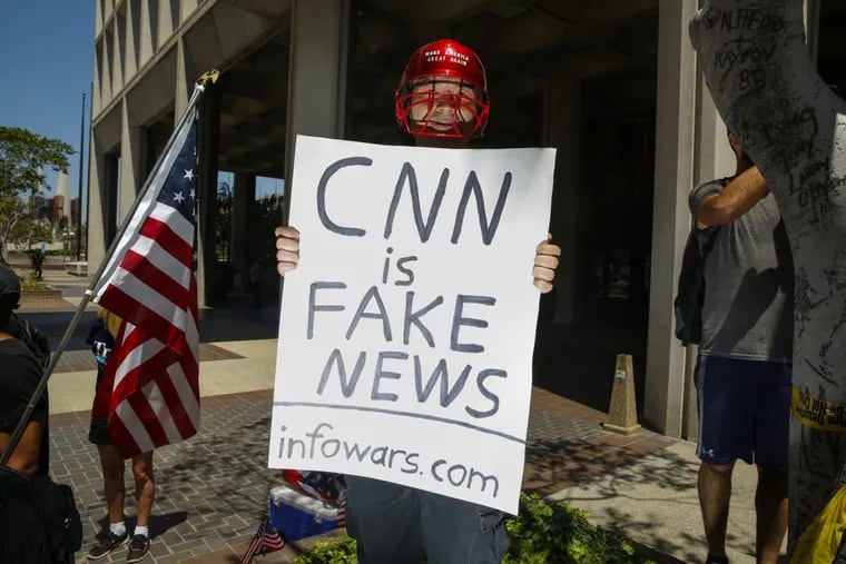 A man holding a sign that says, &quot;CNN is Fake News&quot; and &quot;infowars.com&quot; positioned himself into photos while the media covered an Impeachment March in downtown Los Angeles on July 2, 2017.