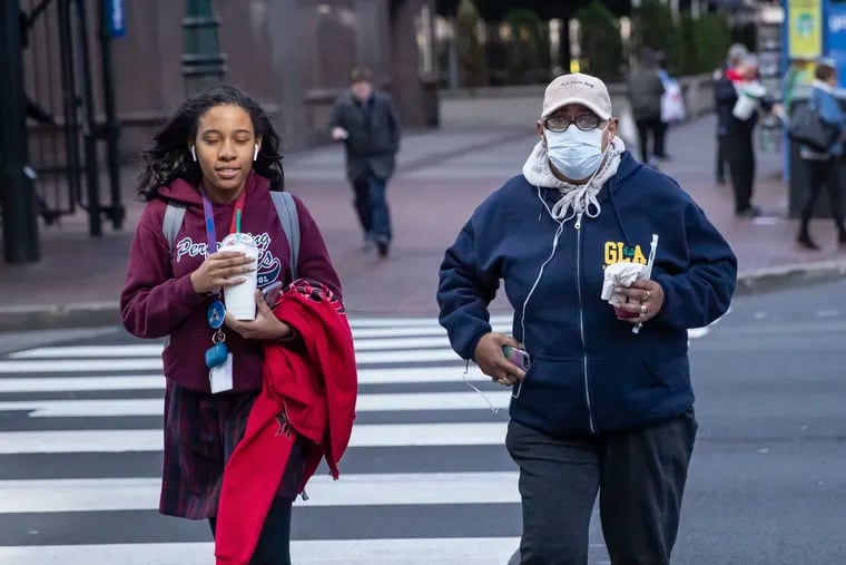 Judy Perry, right, from Philadelphia, wears a surgical mask as protection against the COVID-19 virus, as she crosses Market Street on March 10, 2020. Perry has a heart condition and trouble breathing so she is taking every precaution against the virus that she can.