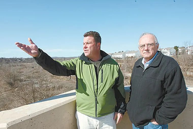 Manny Demutis, left, and Barry Cassidy stand on the Gay Street Bridge in Phoenixville as they talk about the minor league baseball stadium they hope to build in the area behind them. (Charles Fox / Staff Photographer)